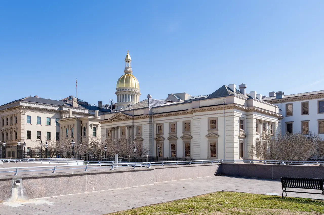The New Jersey State House in Trenton, a cream stone building with a gold dome, under a clear blue sky