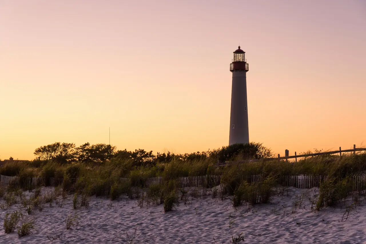 Cape May Lighthouse at sunset, above dune grass and a sand fence