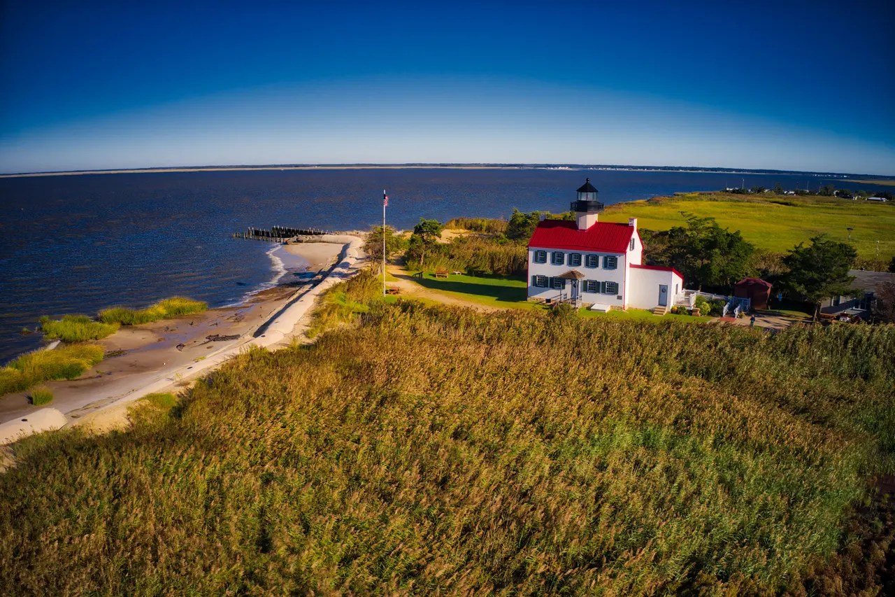 East Point Lighthouse, a white house with a red roof and a lantern, on a marsh beside Delaware Bay, seen from the air
