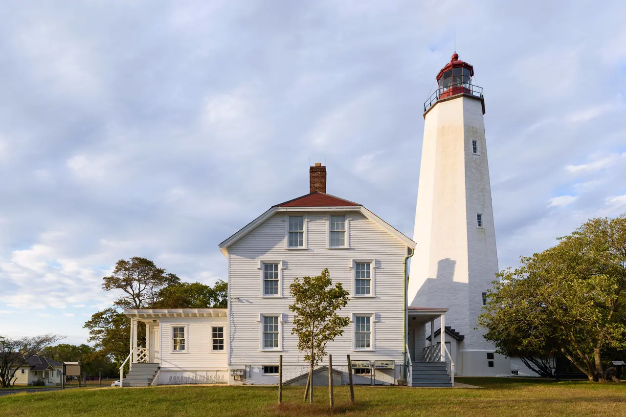 Sandy Hook Lighthouse, a white stone tower with a red lantern, beside the white keeper's house